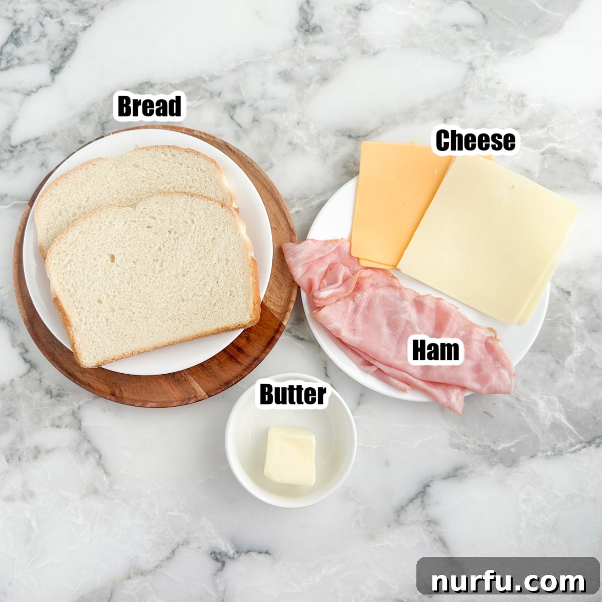 Ultimate Ham and Cheese Melt 3 A selection of grilled ham and cheese sandwich ingredients: bread, sliced cheese, deli ham, and softened butter, laid out on a plate.