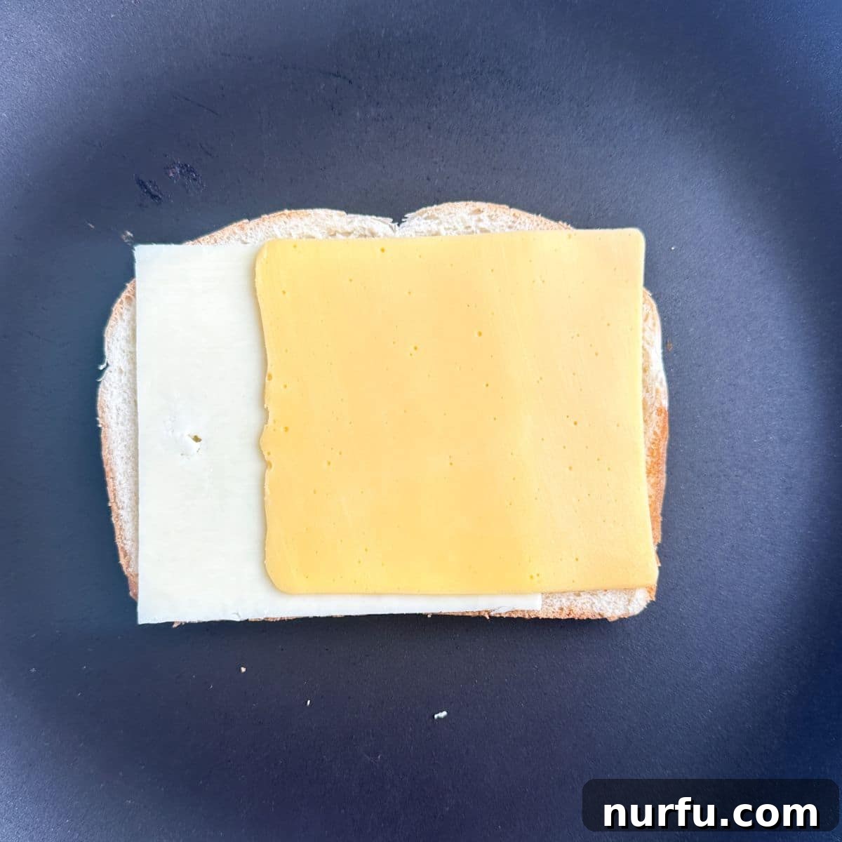 Ultimate Ham and Cheese Melt 5 A slice of bread placed butter-side down in a skillet, topped with two slices of cheese, ready for the ham layer.
