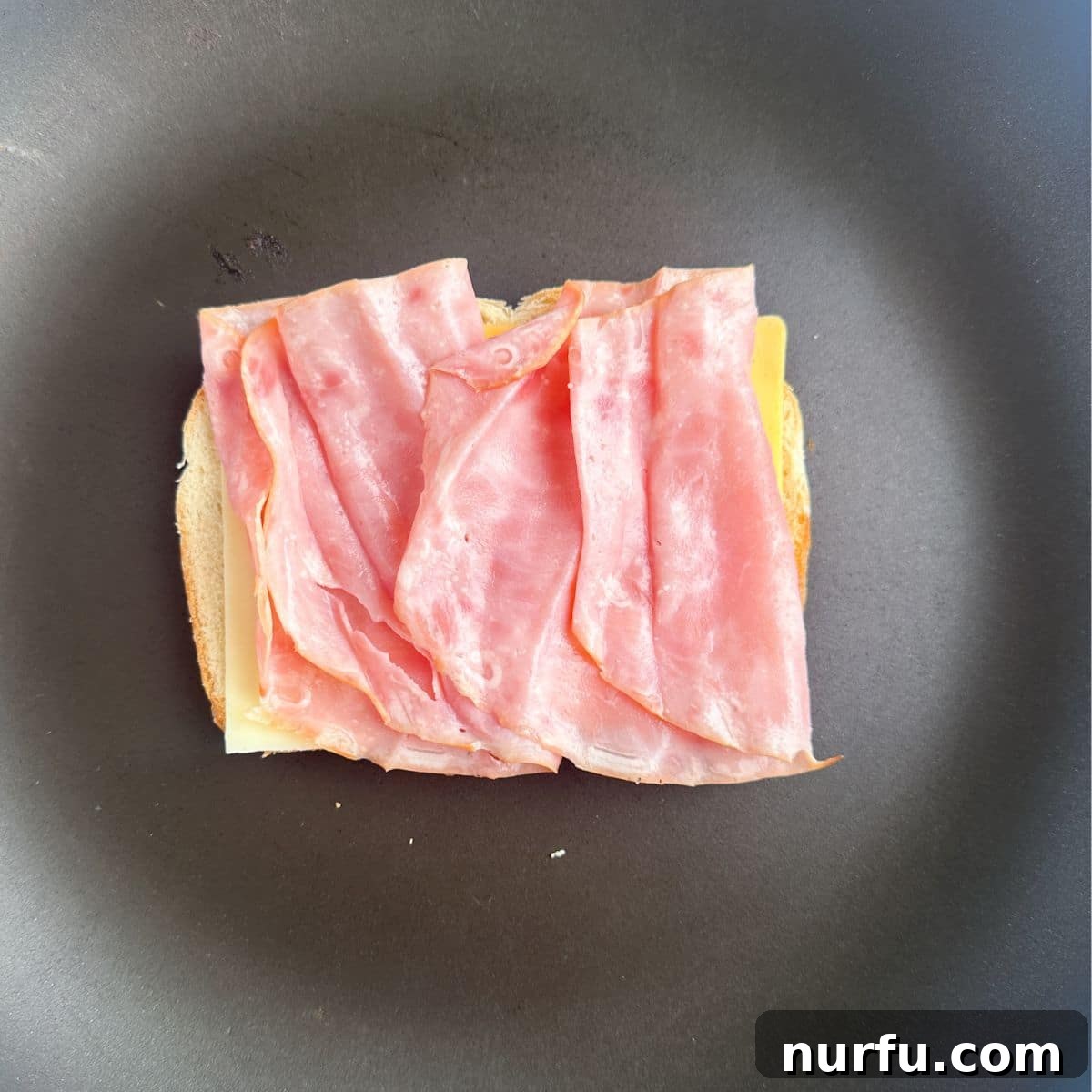 Ultimate Ham and Cheese Melt 6 A slice of bread in a skillet, layered with cheese and deli ham, demonstrating the sandwich assembly.