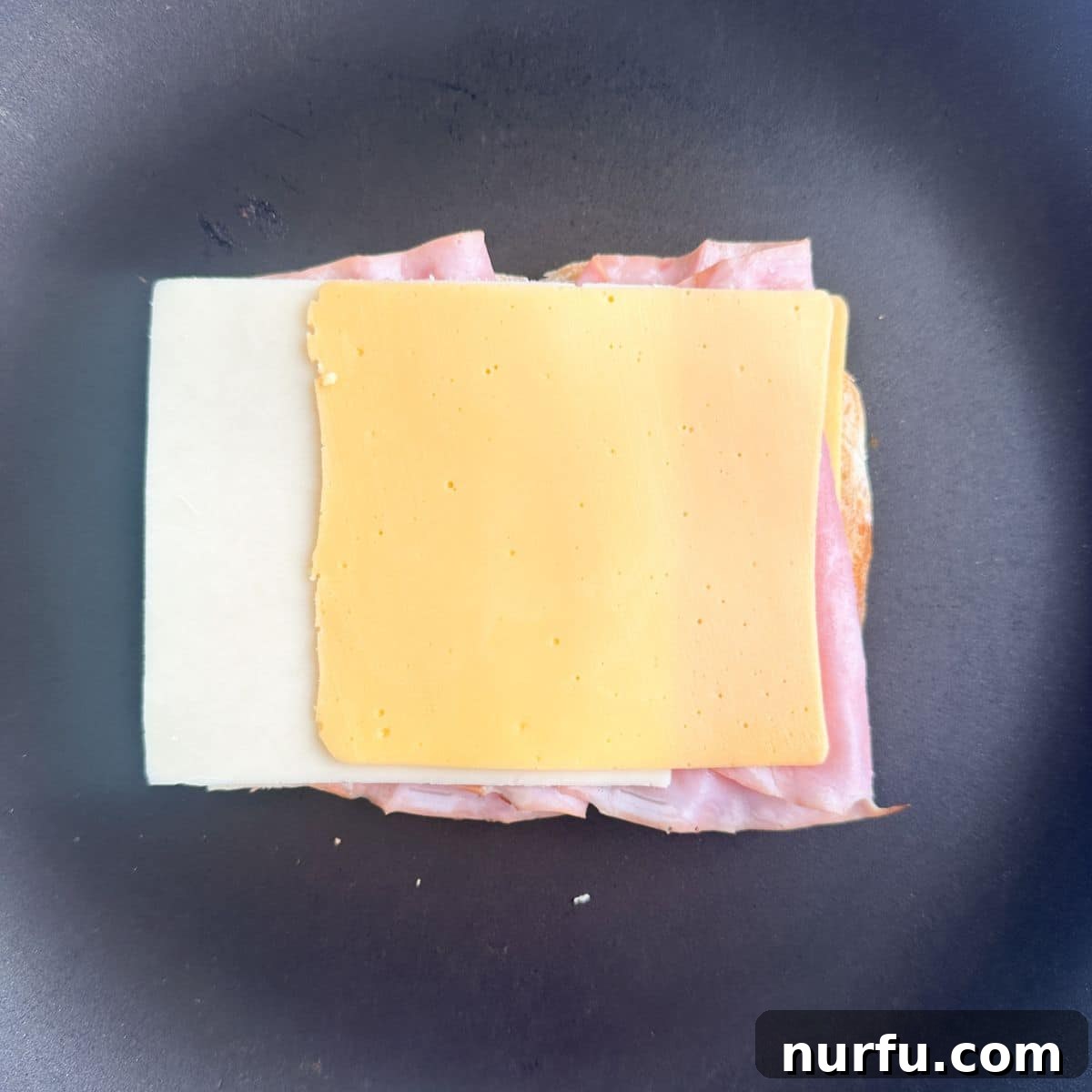 Ultimate Ham and Cheese Melt 7 The final layer of cheese being placed on top of the ham and bread, completing the sandwich stack.