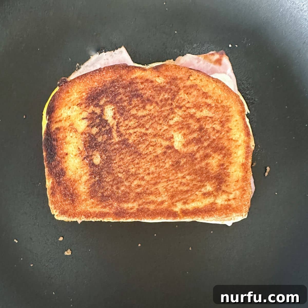 Ultimate Ham and Cheese Melt 8 A assembled grilled ham and cheese sandwich cooking in a skillet, with one side already golden brown and ready to flip.