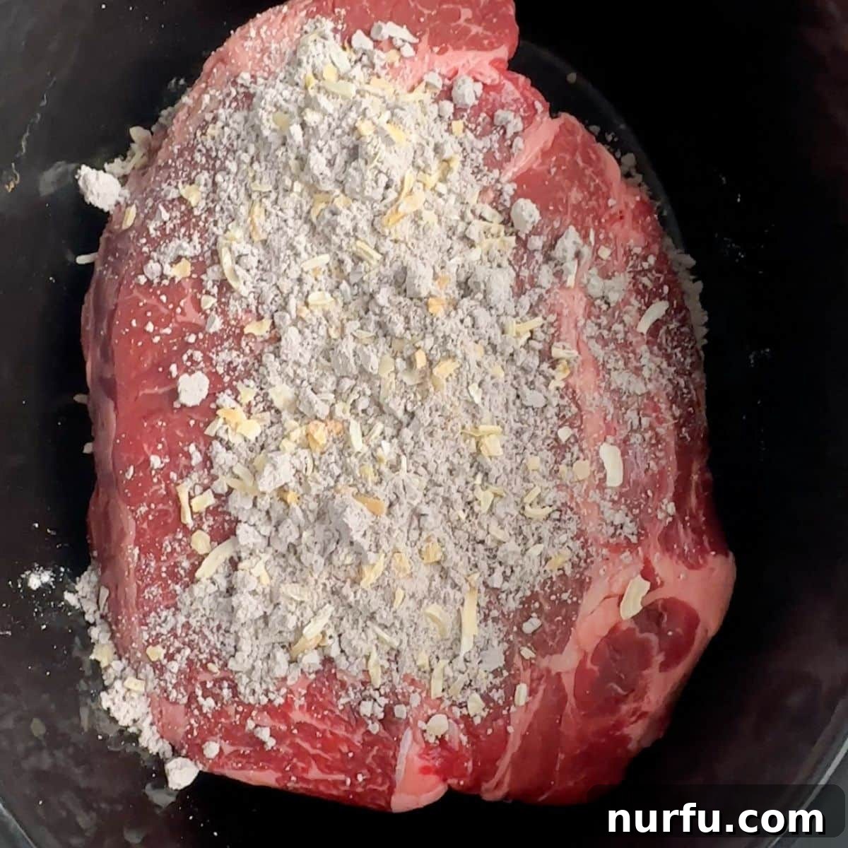 Fall Apart Slow Cooker BBQ Beef 4 A raw chuck roast sitting inside a slow cooker, with a generous layer of dry onion soup mix sprinkled over its surface, ready for the next steps.