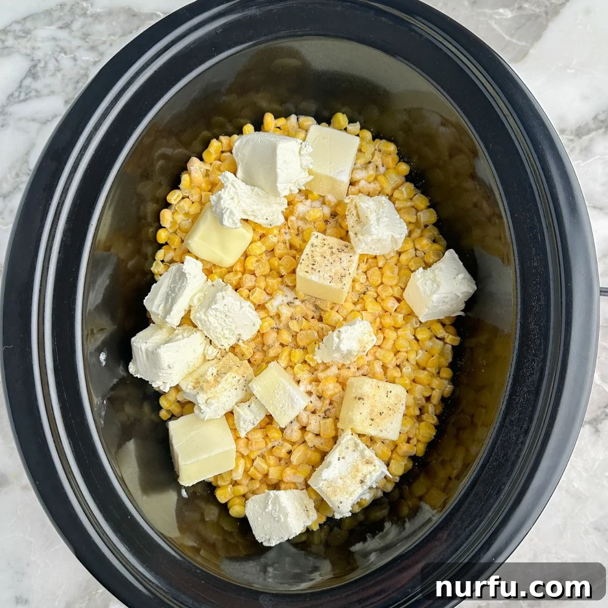 Dreamy Slow Cooker Cream Cheese Corn 4 The initial stage of preparation within a slow cooker, showing vibrant frozen corn kernels, neatly cut cream cheese cubes, and pats of butter layered together, poised for the cooking process to begin.