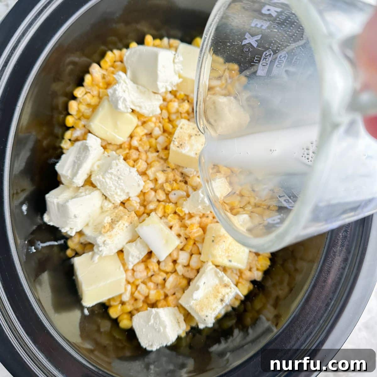Dreamy Slow Cooker Cream Cheese Corn 5 A closer view inside the slow cooker, illustrating the final mixture before cooking: half and half has been poured over the corn, cream cheese, and butter, creating a cohesive blend of ingredients ready to transform into creamy perfection.