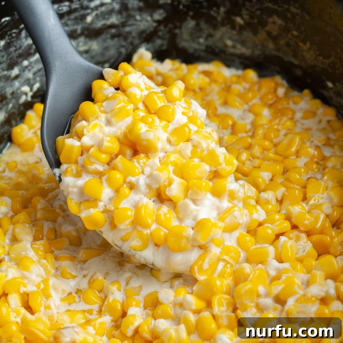Dreamy Slow Cooker Cream Cheese Corn 6 A wooden spoon scooping a generous portion of warm, velvety slow cooker cream cheese corn from a large white serving bowl, highlighting its rich, creamy texture and delicious appeal.