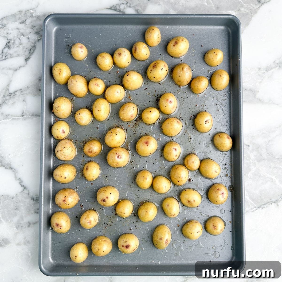 Small potatoes cut in half and arranged cut-side down on a baking sheet, ready for roasting.