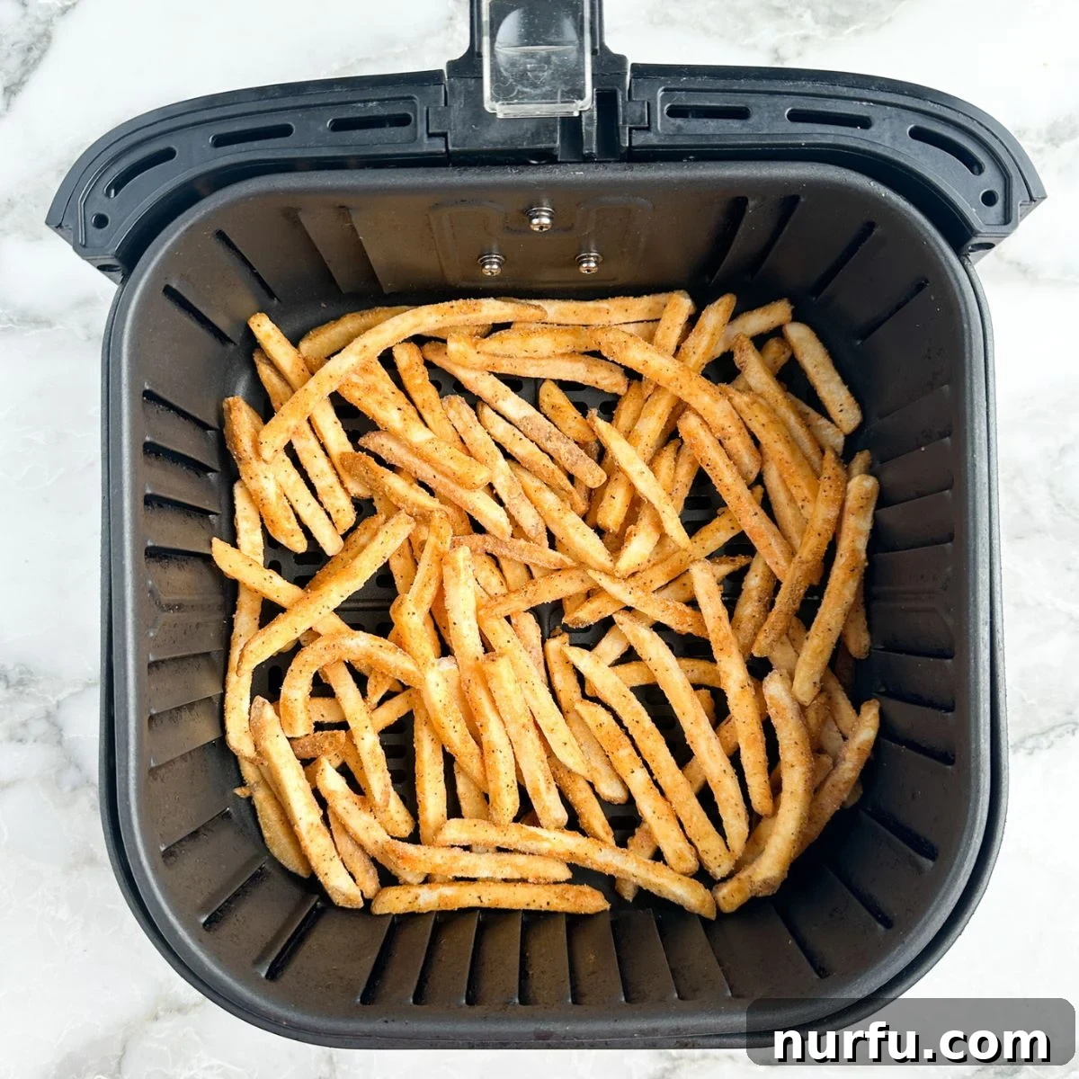 Crispy Checkers Fries in the Air Fryer 4 Frozen french fries spread out in an air fryer basket.