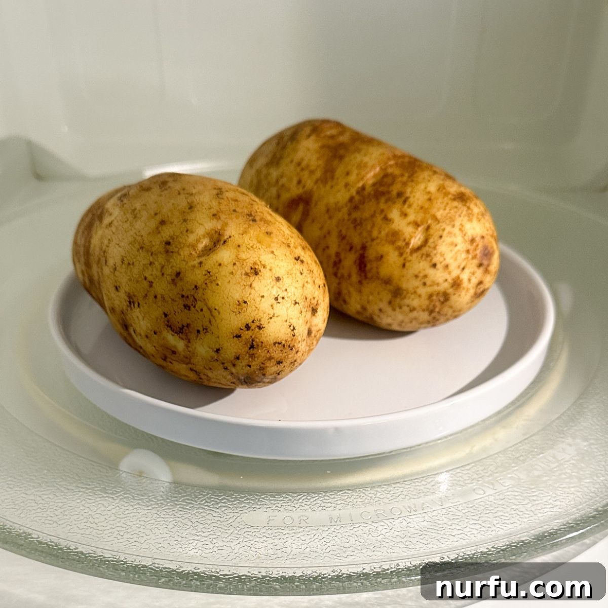 Two potatoes on a plate inside a microwave, illustrating the cooking process.
