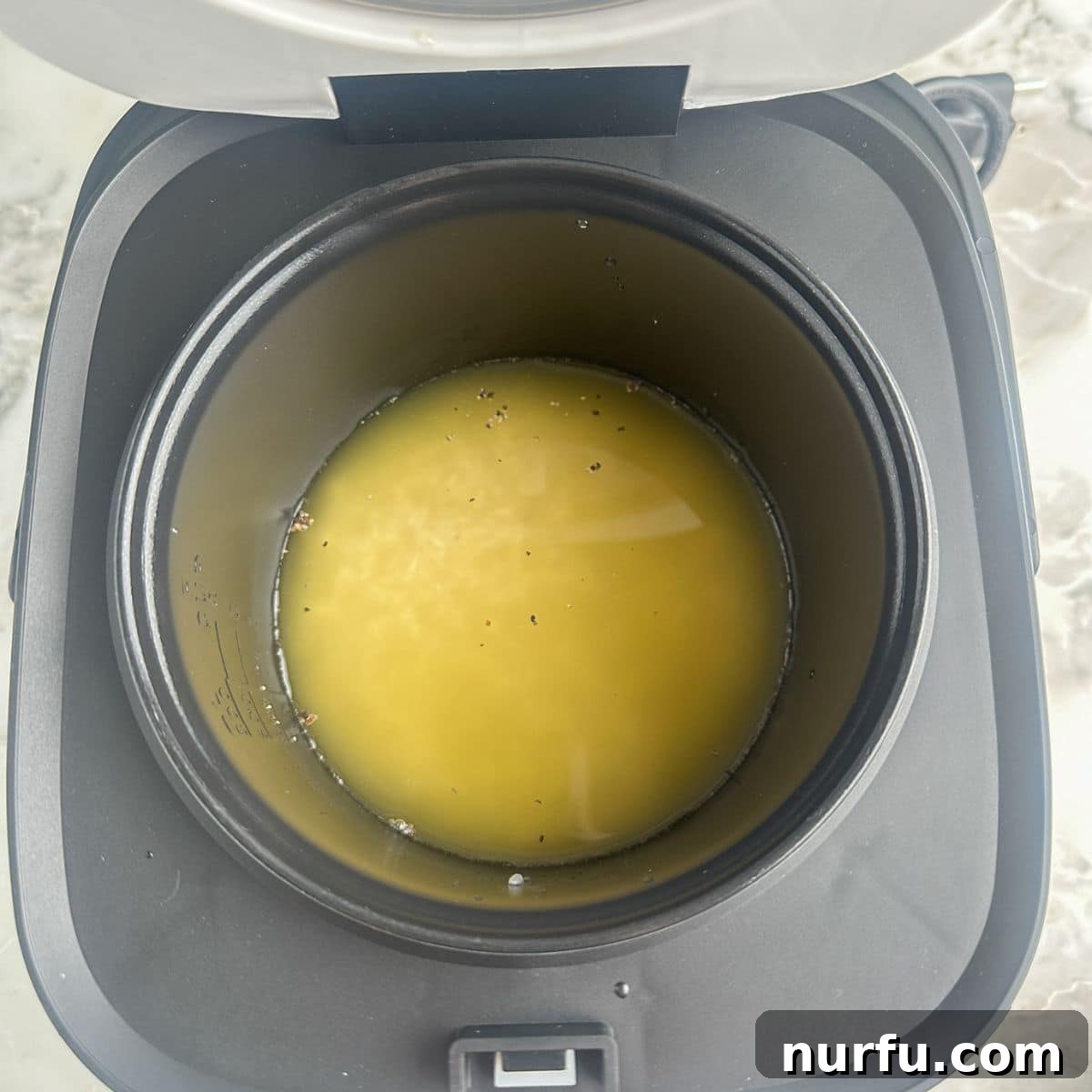 Creamy Cheesy Rice Cooker Perfection 4 Rice cooker with uncooked rice and chicken broth ready to be cooked.