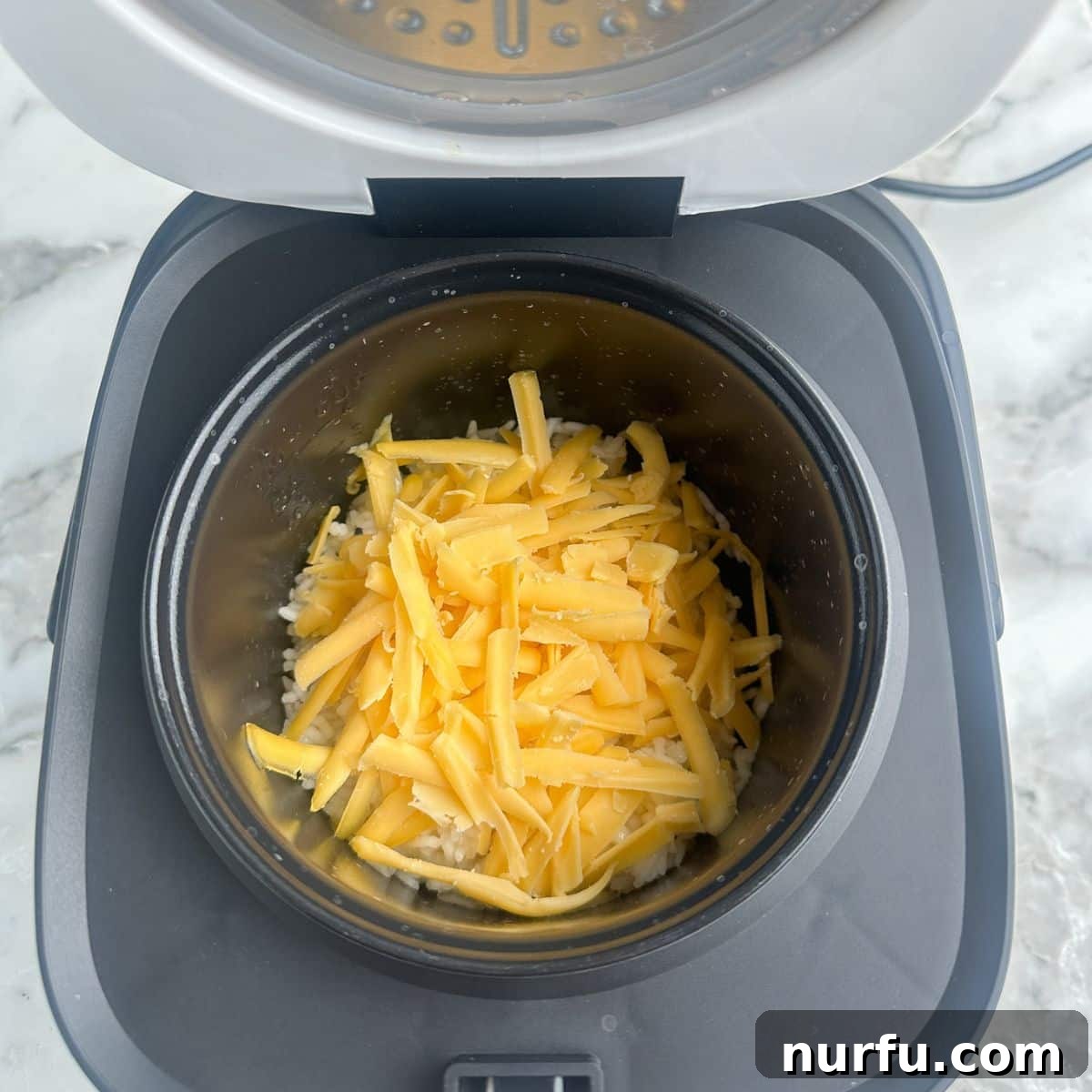 Creamy Cheesy Rice Cooker Perfection 5 Hot, cooked rice with shredded cheese added in a rice cooker, ready to be melted.