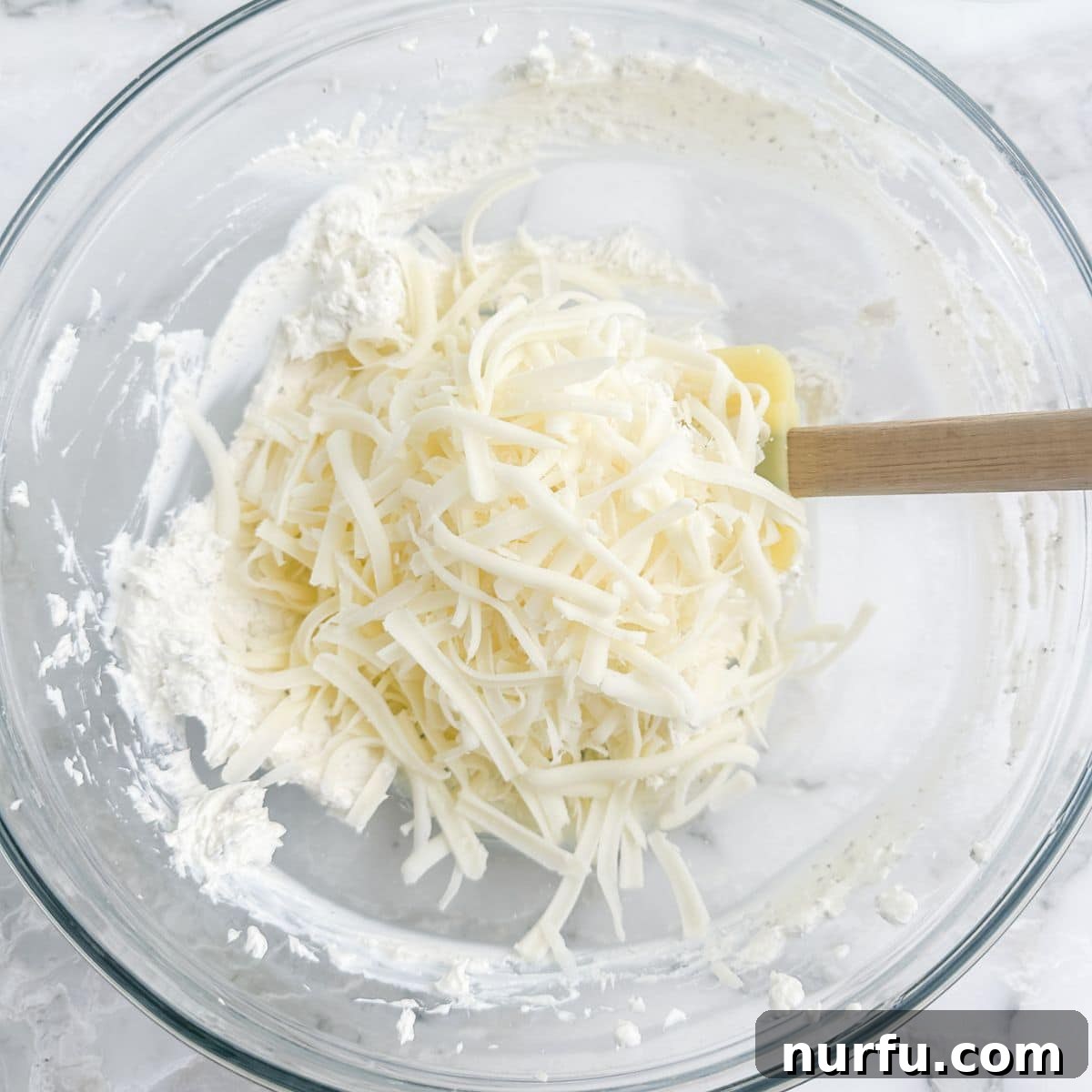 Ultimate Party Pizza Dip 4 A bowl containing a creamy mixture of softened cream cheese and shredded mozzarella, ready for the next step in making pizza dip.