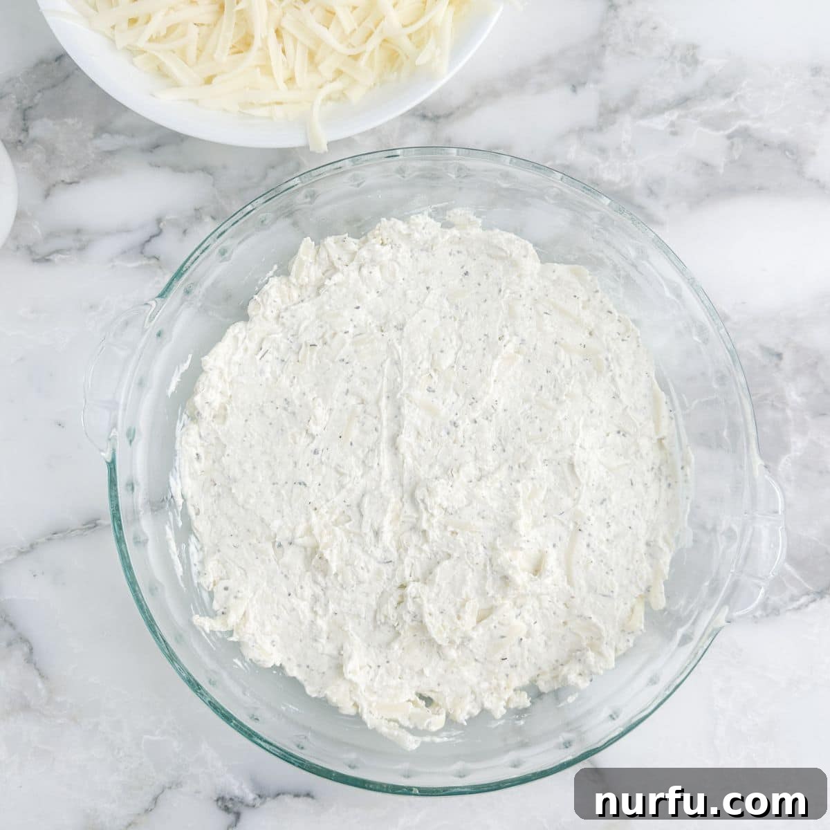 Ultimate Party Pizza Dip 5 A smooth, creamy dip base spread evenly in a pie plate, forming the foundation of the pizza dip before adding sauce and toppings.