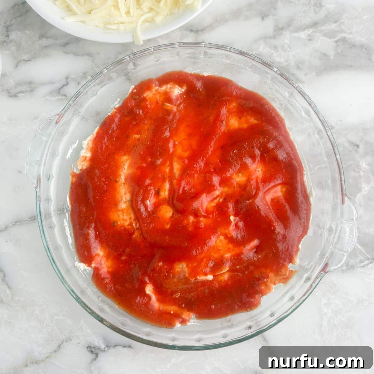 Ultimate Party Pizza Dip 6 A pie dish with a creamy base topped with a smooth layer of marinara sauce, preparing for the final cheese and pepperoni layers.