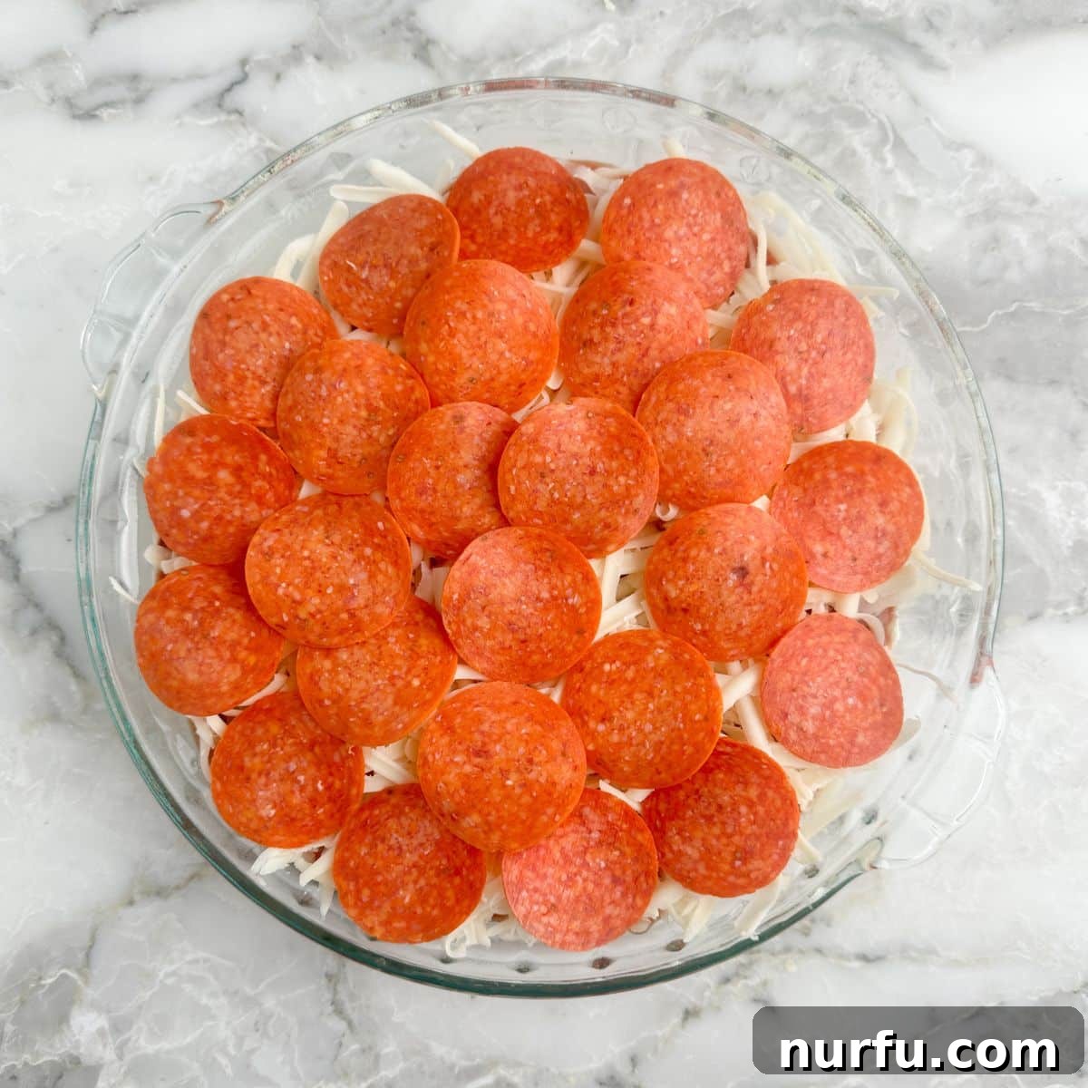 Ultimate Party Pizza Dip 7 A pie dish filled with a finished pizza dip, hot from the oven, with melted cheese and crispy pepperoni on top, ready for serving.