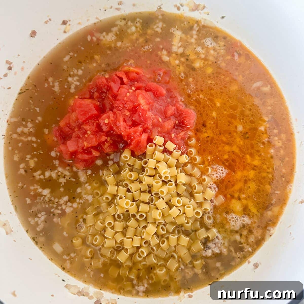 Velvety Italian Sausage and Parmesan Soup 5 A pot on the stove with chicken broth, petite diced tomatoes, and ditalini pasta simmering.