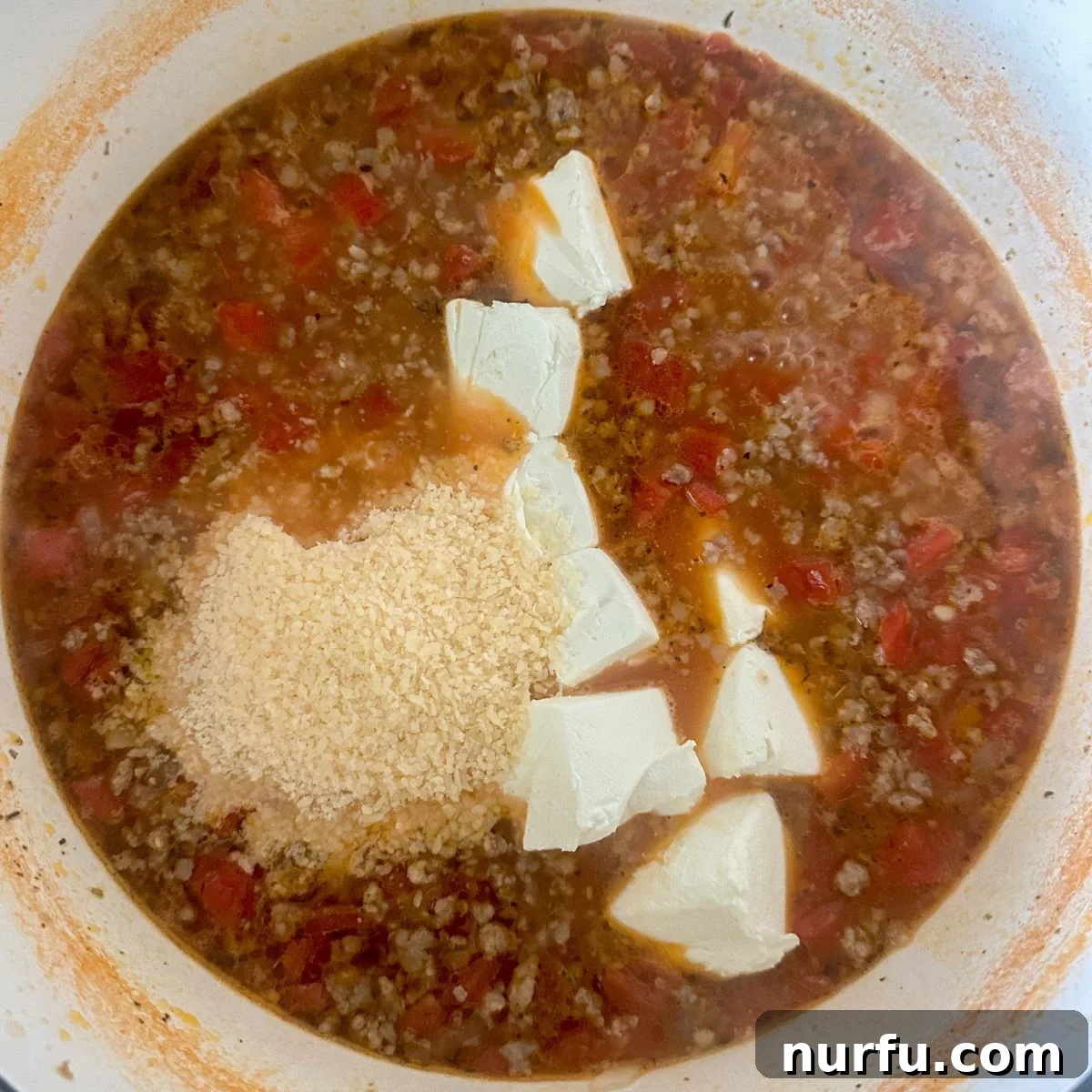 Velvety Italian Sausage and Parmesan Soup 6 A pot of creamy Italian sausage soup on the stove, with cream cheese and grated Parmesan just added and being stirred in.