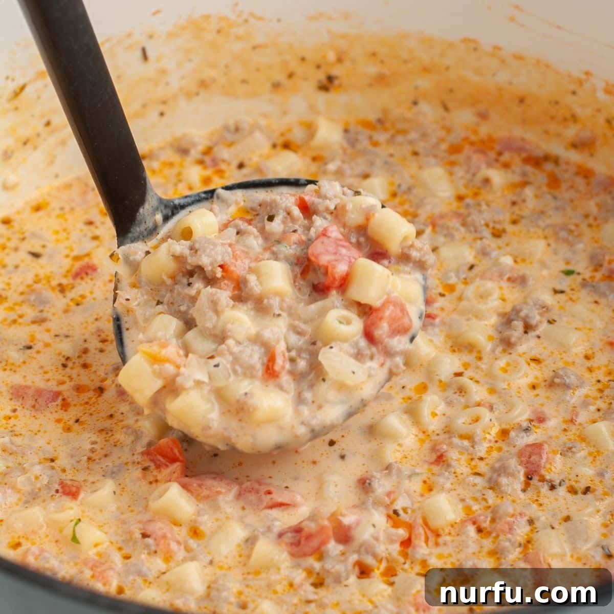 Velvety Italian Sausage and Parmesan Soup 7 A ladle scooping a generous portion of creamy Italian sausage and pasta soup from a pot.