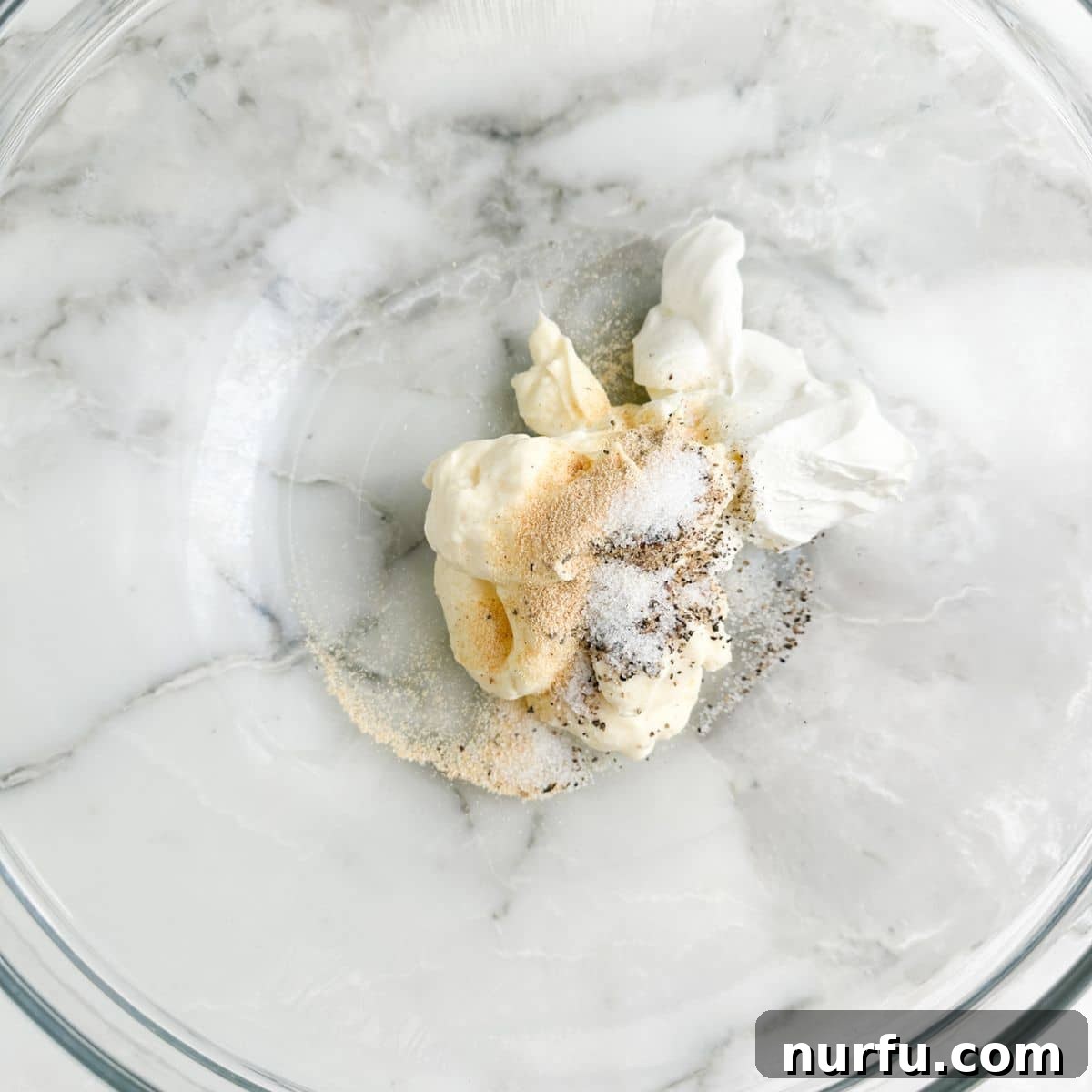 Deep South Mud Pie Potatoes 4 A mixing bowl filled with mayonnaise, sour cream, and a blend of seasonings, whisked to a smooth consistency.