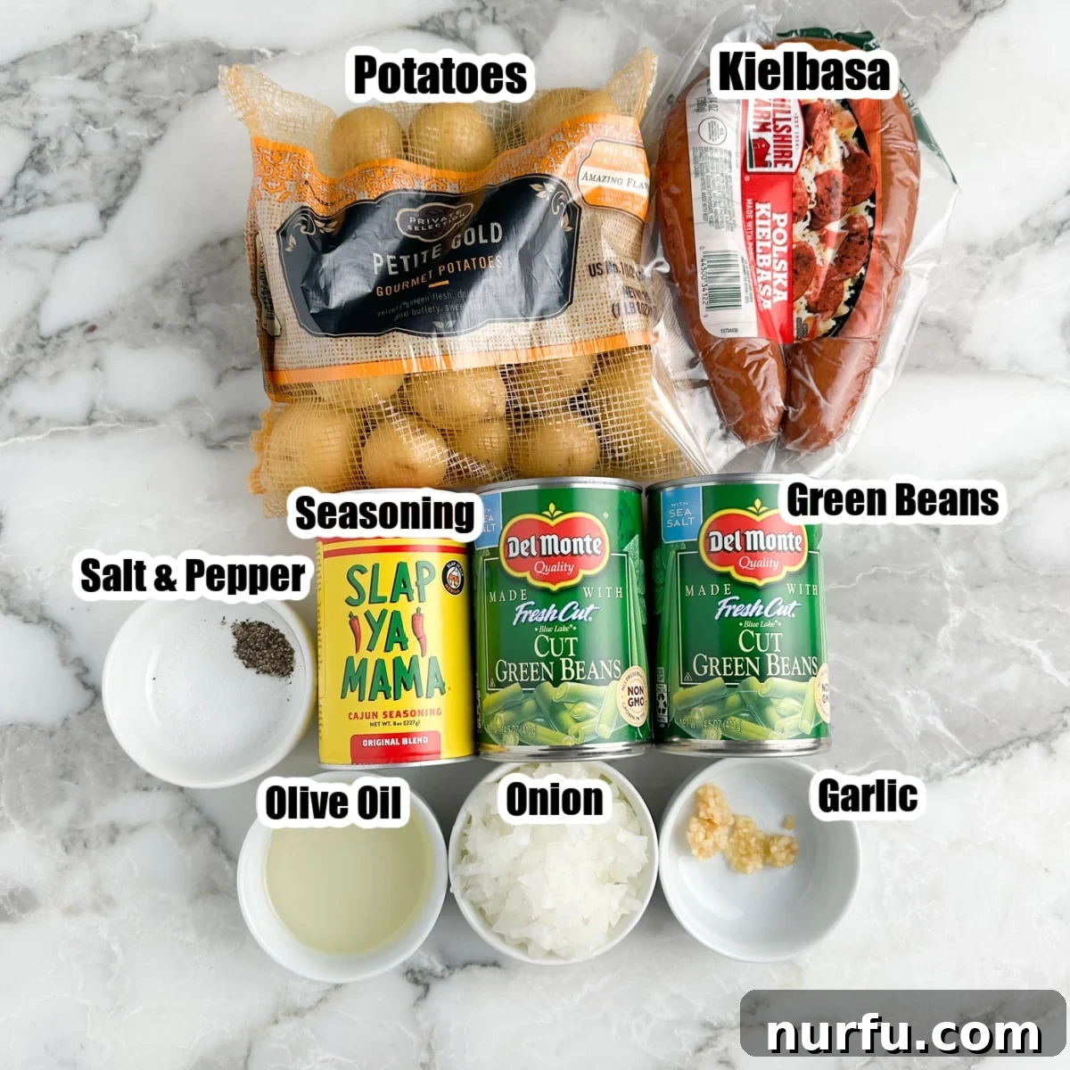 Hearty Sausage Green Bean Potato Oven Bake 3 A flat lay photograph displaying all the fresh ingredients needed for Sausage Green Bean Potato Casserole: a bag of small potatoes, kielbasa sausage, canned green beans, diced onion, a whole garlic bulb, olive oil, and a bottle of Cajun seasoning.