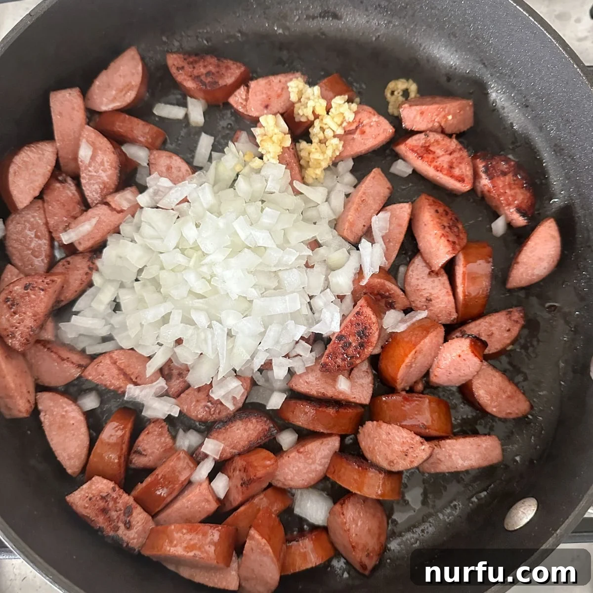 Hearty Sausage Green Bean Potato Oven Bake 4 Sliced kielbasa sausage and diced onion cooking in a large skillet.
