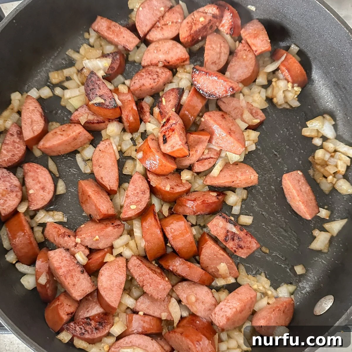 Hearty Sausage Green Bean Potato Oven Bake 5 Kielbasa sausage and diced onion continue to cook in a skillet, turning golden brown.