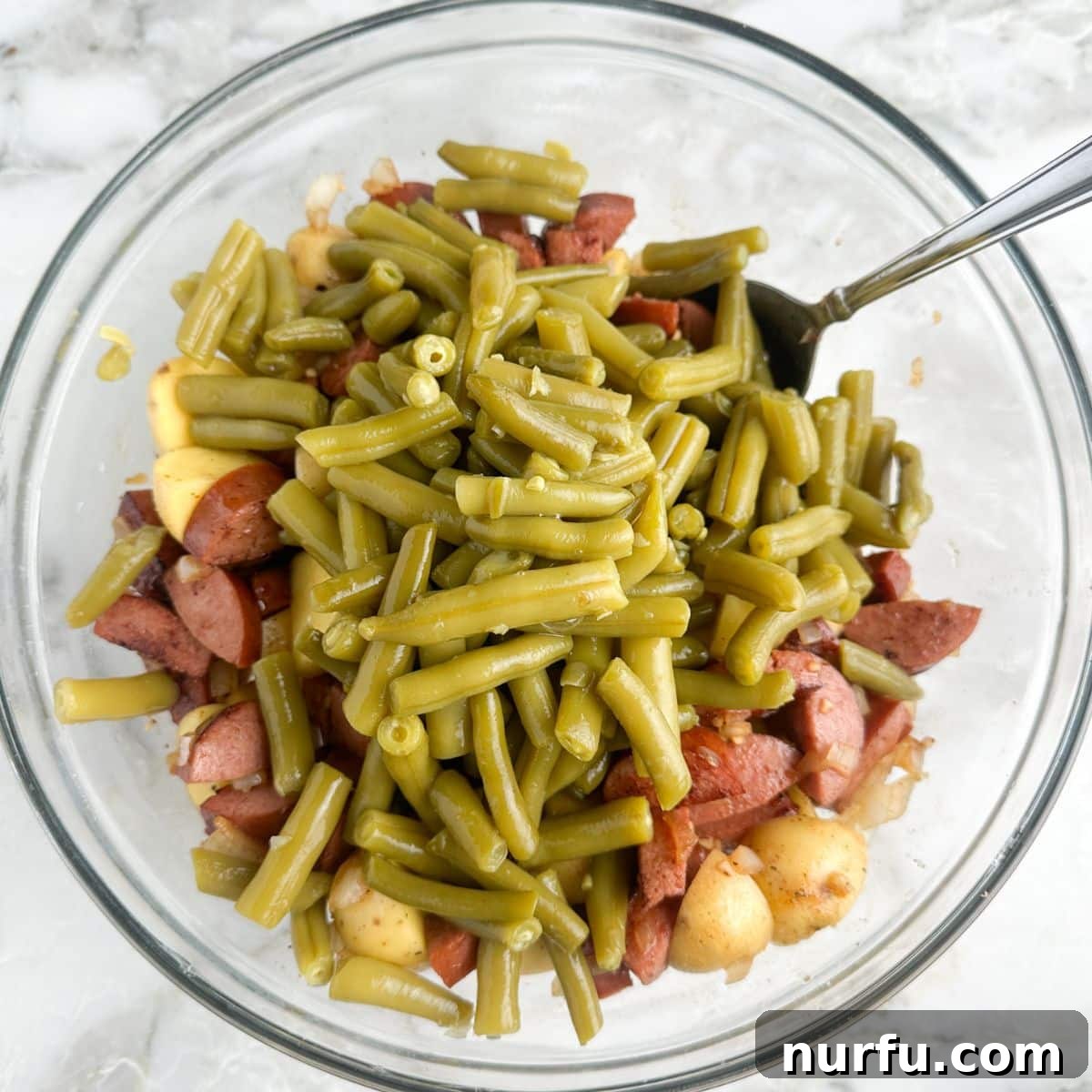 Hearty Sausage Green Bean Potato Oven Bake 7 A large mixing bowl containing a colorful mixture of seasoned potatoes, cooked kielbasa, and green beans, ready for baking.