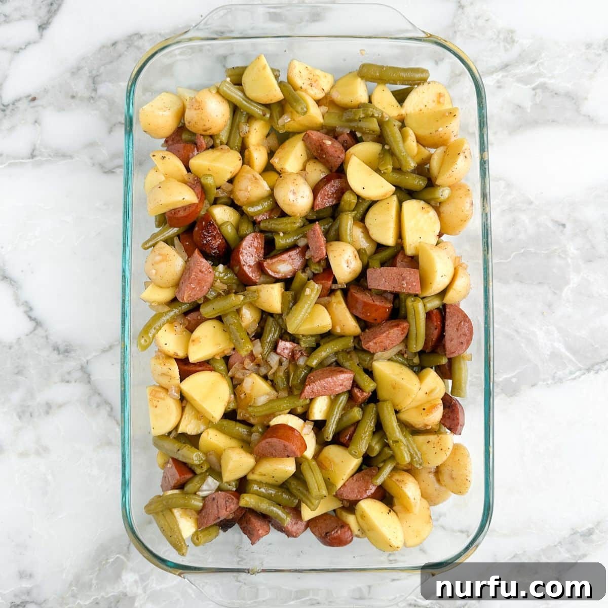 Hearty Sausage Green Bean Potato Oven Bake 8 A casserole dish filled with potatoes, kielbasa sausage, and green beans, covered with foil, ready to be baked in the oven.