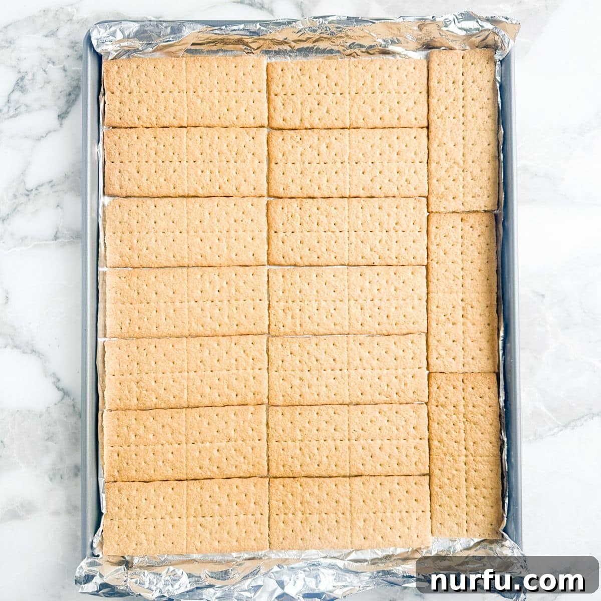 A baking sheet lined with aluminum foil, neatly covered with a single layer of honey graham crackers.
