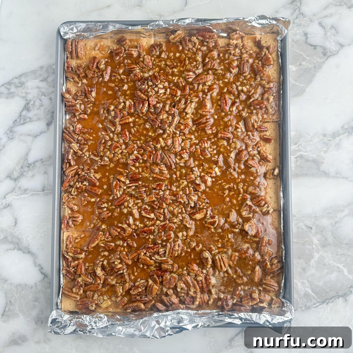 A baking sheet filled with graham crackers covered in a golden-brown pecan mixture, fresh out of the oven.