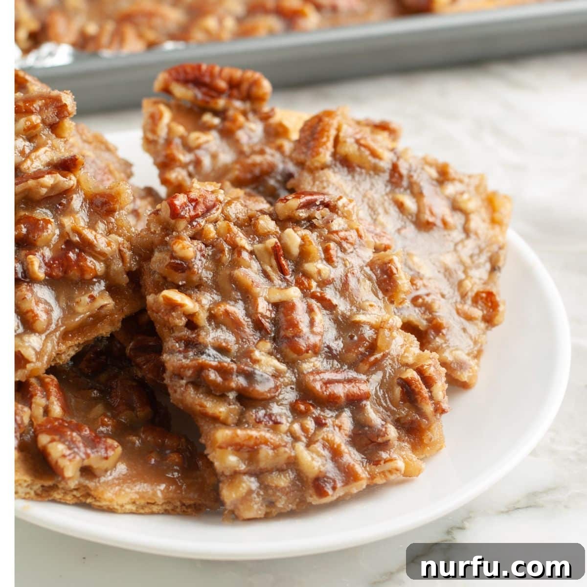 A rustic wooden plate filled with irregularly shaped pieces of golden-brown pecan pie bark, ready for serving.
