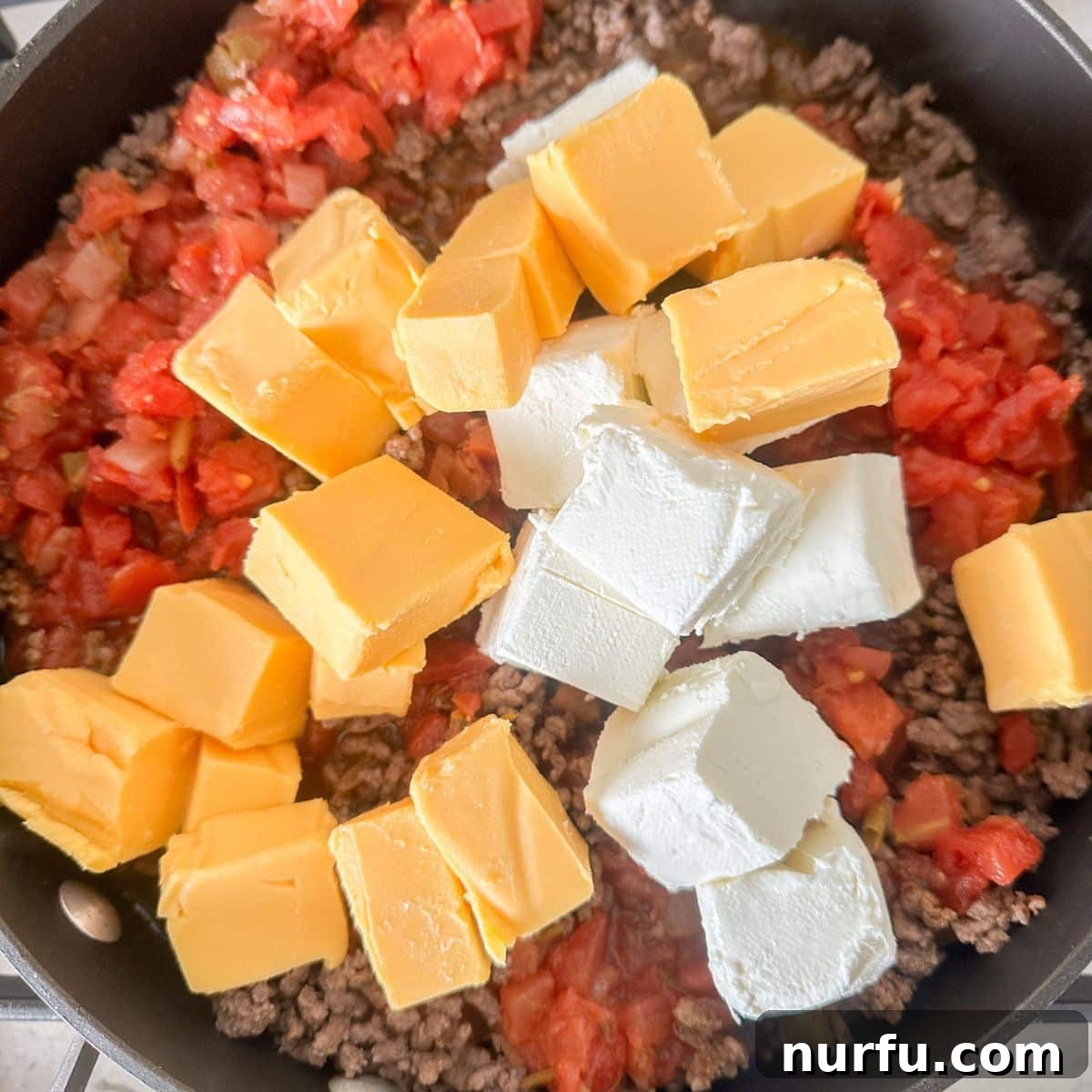 Savory Burger Dipping Sauce 5 A vibrant mix of seasoned ground beef, zesty diced tomatoes, and cubed Velveeta and cream cheese melting together in a skillet, creating a rich base for hamburger dip.