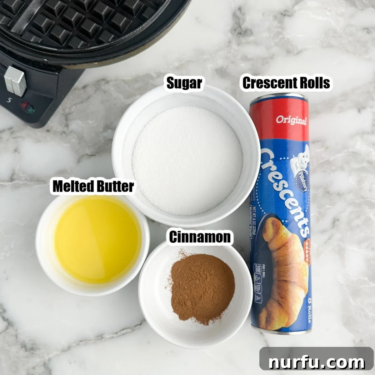 Close-up of ingredients for croffles: a can of crescent rolls, a bowl of granulated sugar, a smaller bowl of ground cinnamon, and a stick of unsalted butter.