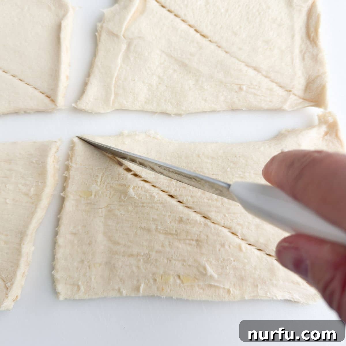 A hand carefully cutting pre-perforated crescent roll dough into individual triangles on a cutting board.