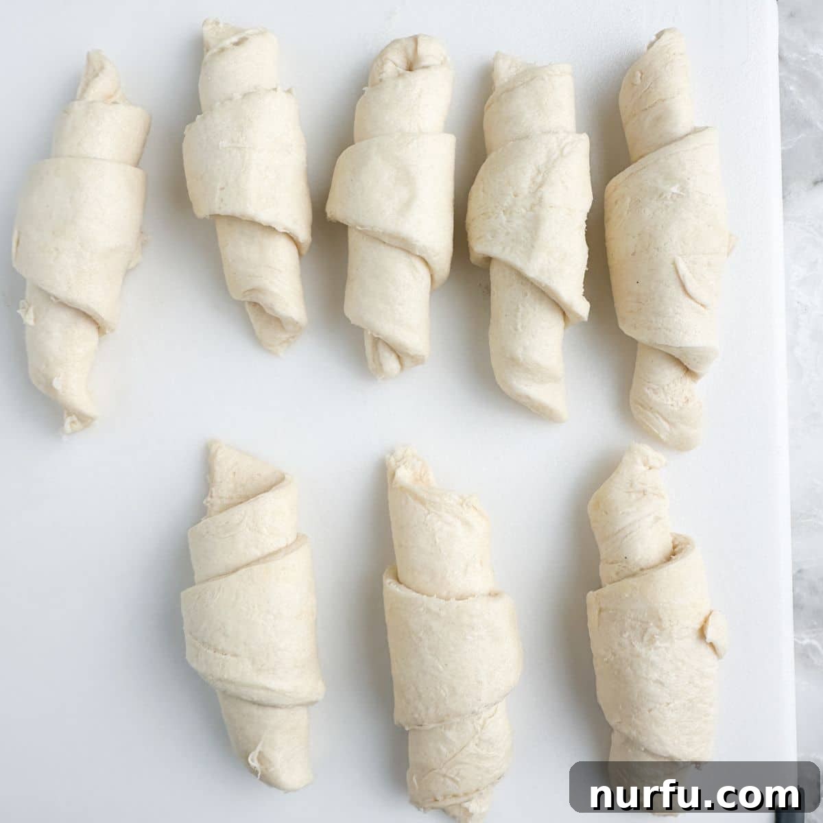 A plate filled with several uncooked crescent rolls, perfectly rolled and ready for the next step.