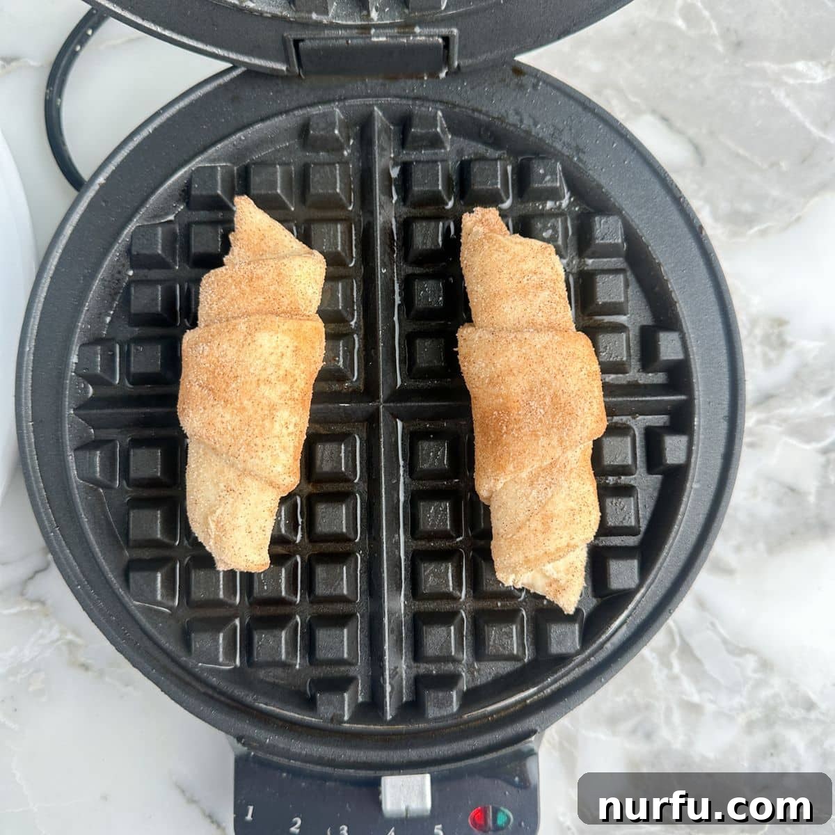 Two crescent rolls placed on a preheated and greased waffle iron, ready to be cooked.