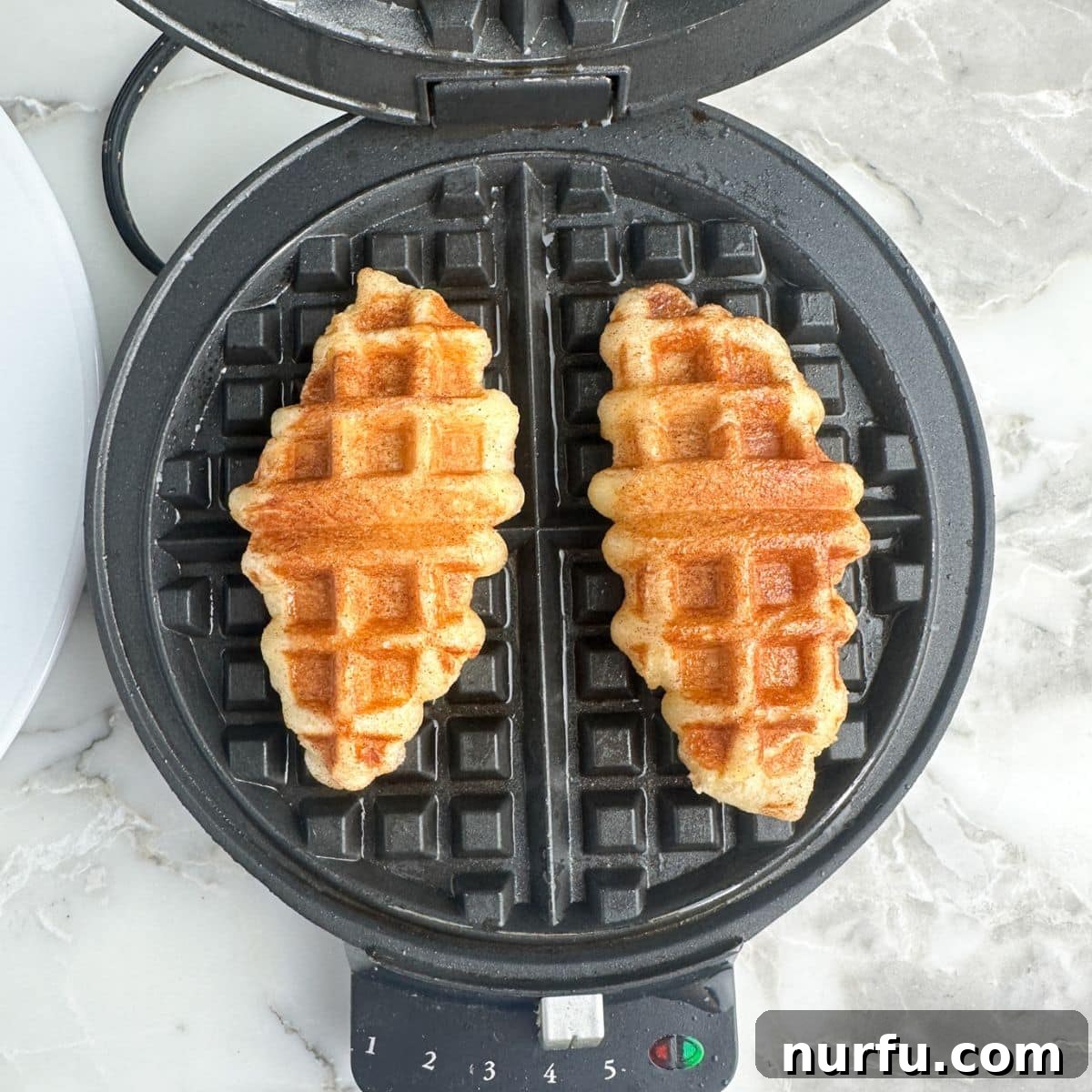 Golden-brown, freshly cooked croffles resting on the waffle iron, showcasing their crispy texture and sugar coating.