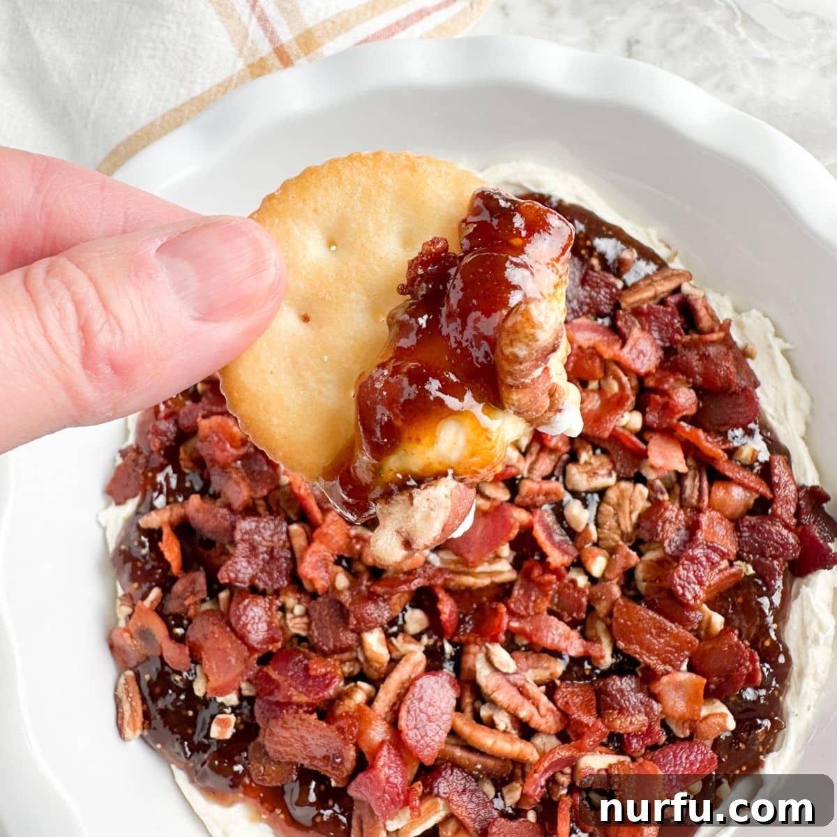 Fig & Bacon Boursin Bliss 2 Cracker generously topped with creamy Boursin, fig jam, crispy bacon, and chopped pecans, held in a hand against a rustic background.