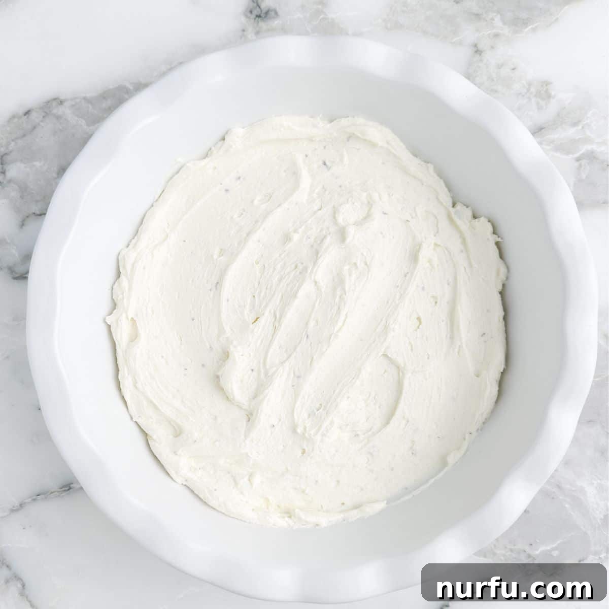 Fig & Bacon Boursin Bliss 6 A pie plate with the smooth, whipped cream cheese and Boursin cheese mixture spread evenly at the bottom, ready for toppings.