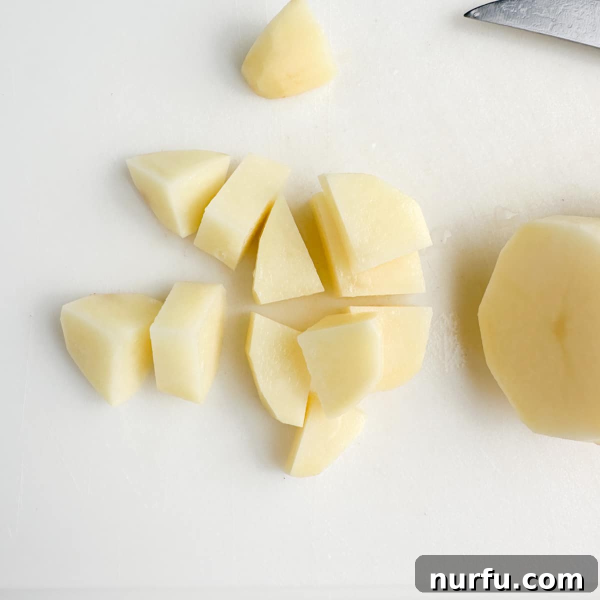 Velvety Boursin Garlic Herb Mash 4 Freshly cut potato chunks on a cutting board, ready for boiling.