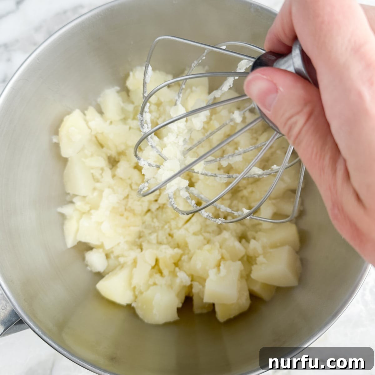 Velvety Boursin Garlic Herb Mash 5 Partially mashed potatoes in a bowl, with softened butter and a block of Boursin cheese added on top.