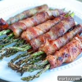 A plate of perfectly cooked bacon-wrapped asparagus spears, showcasing their crisp edges.