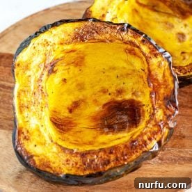 Roasted acorn squash halves on a wooden board, beautifully caramelized.