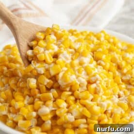 A bowl of rich, creamy corn with a wooden spoon, steaming gently.