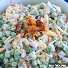A vibrant bowl featuring a creamy pea salad, studded with cheese and bacon.
