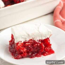 A slice of cranberry JELLO salad topped with a dollop of cream cheese, presented on a plate.