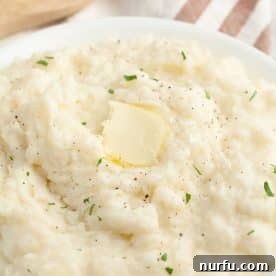 A inviting bowl of rich, creamy mashed potatoes, generously topped with a pat of melting butter.