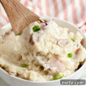 A deep bowl of mashed red skin potatoes, showing off their rustic texture, with a wooden spoon for serving.