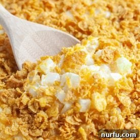 A wooden spoon scooping into a bubbling, cheesy potato casserole, with a crunchy topping.