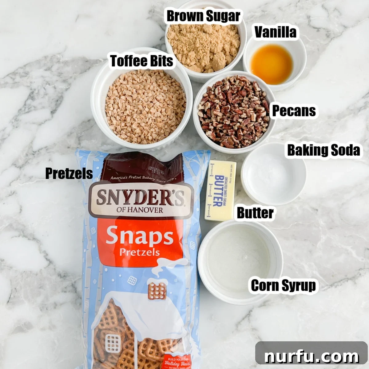 A flat lay arrangement showcasing all the ingredients required for butter toffee pretzels: a bag of pretzels, a bowl of light brown sugar, a bowl of Heath toffee bits, chopped pecans, a stick of butter, and a bottle of light corn syrup, ready for preparation.