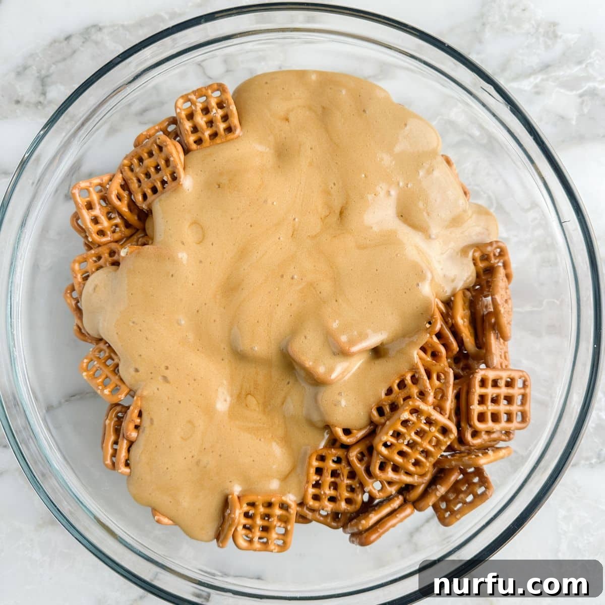 A large mixing bowl filled with pretzels generously coated in a shimmering, sticky butter toffee sauce, mid-toss, ensuring even coverage for every piece.